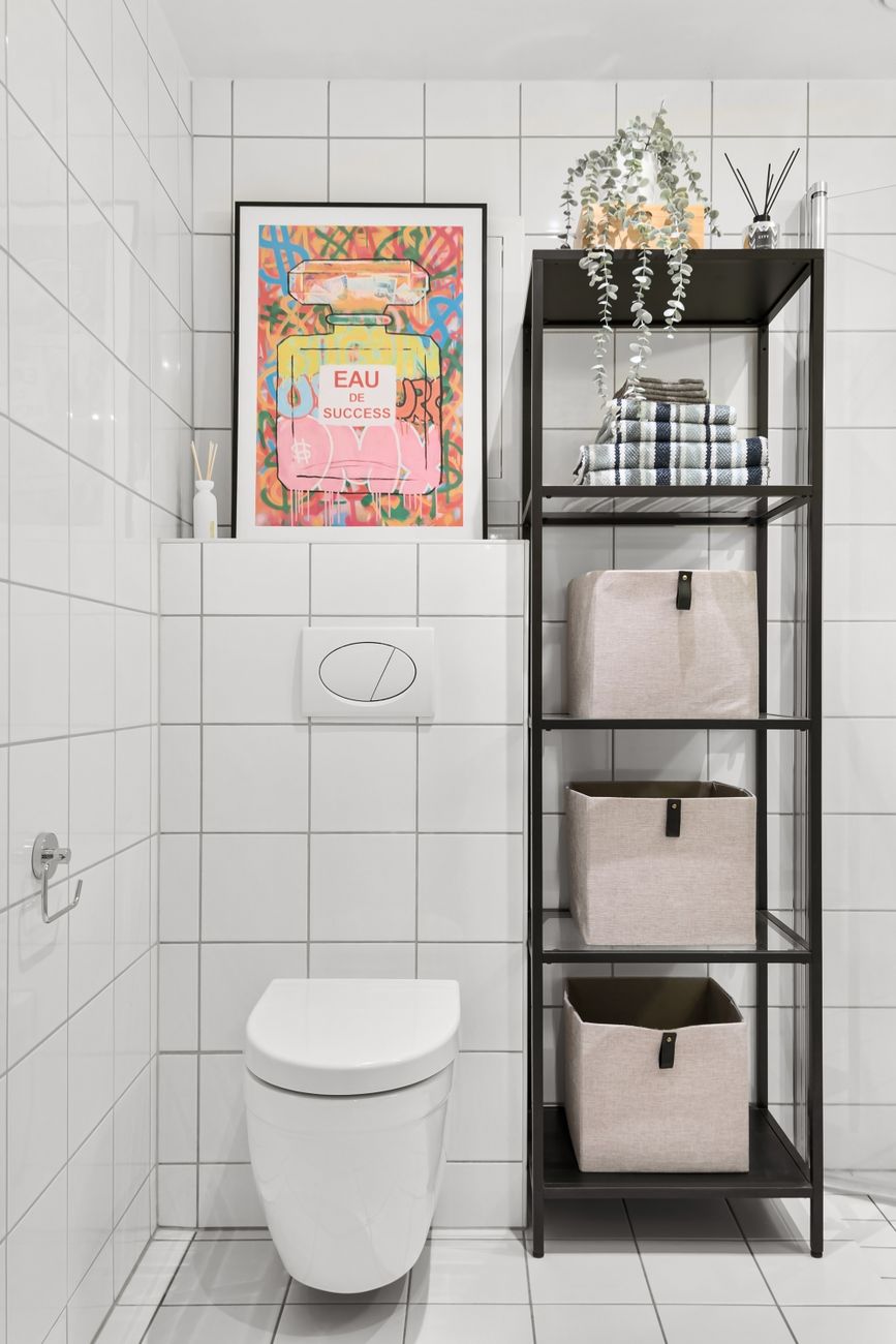Black over-the-toilet shelving unit with storage baskets and towels in a small white-tiled bathroom