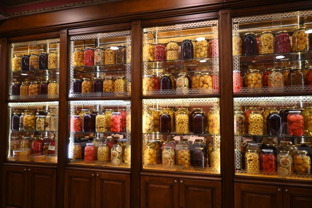 Glass-fronted pantry cabinet with shelves of neatly lined-up jars of preserves and dry food